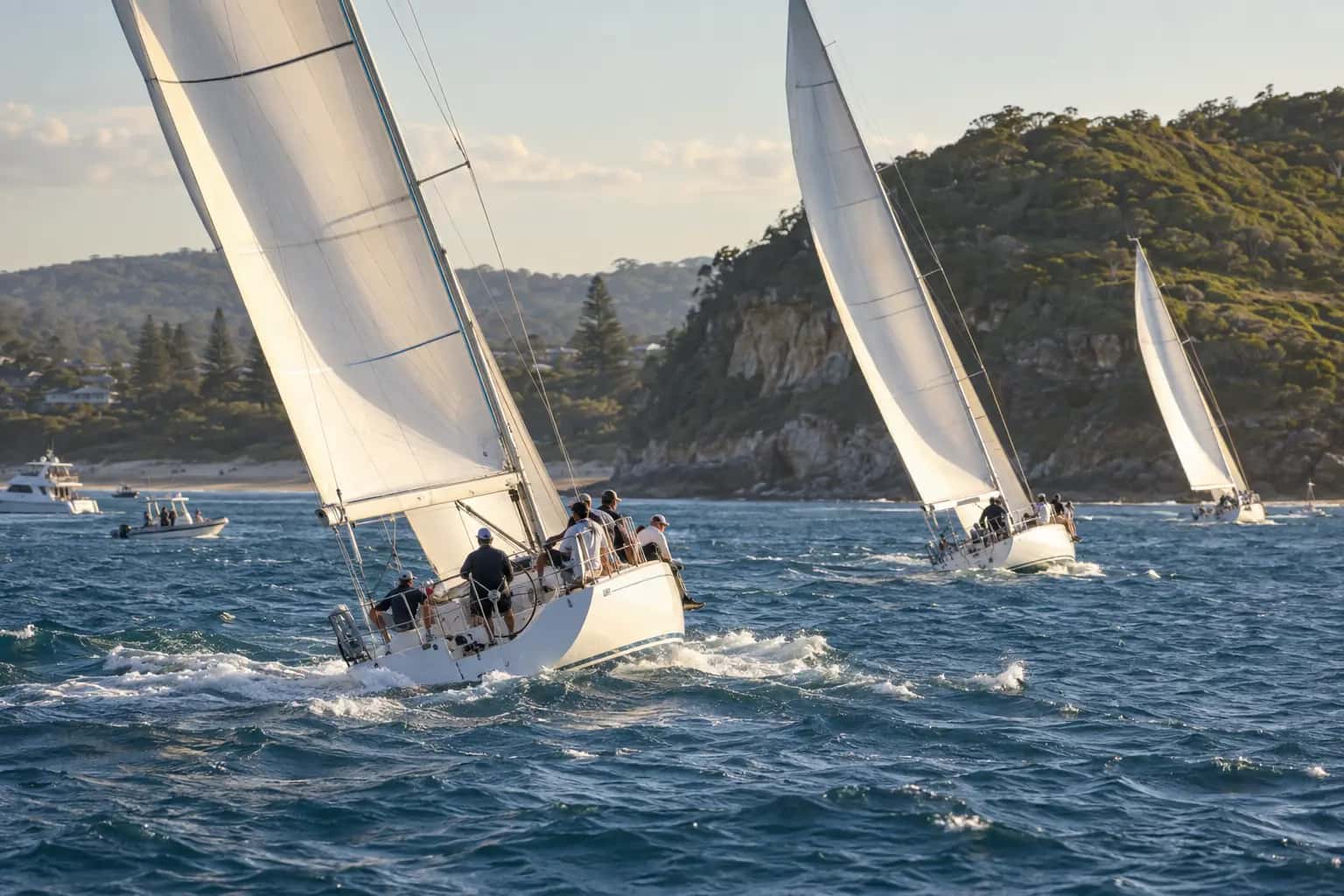 Racing yachts with white sails heeled over on blue water near a green headland